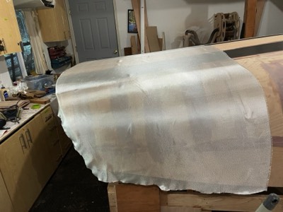  12/11/20 - The first section of fiberglass cloth is laid on the hull. 